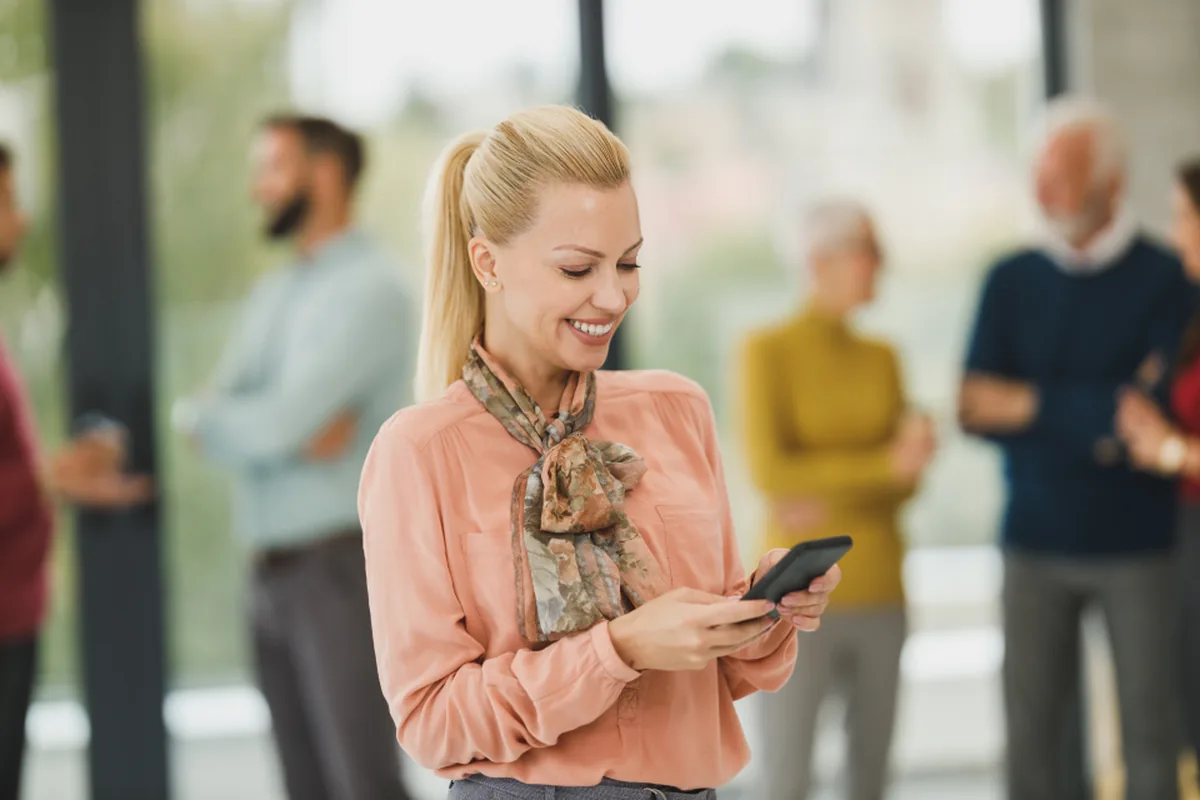 A smiling woman using her phone in a bright office
